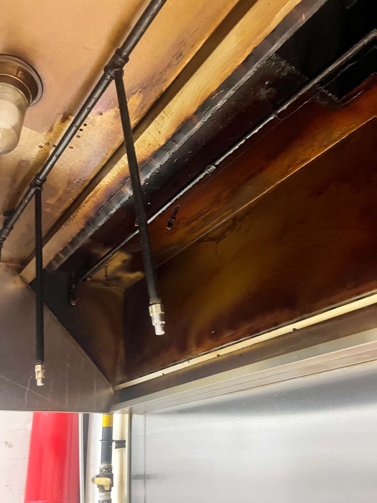 Grease buildup inside the kitchen exhaust system before cleaning — Same hood, same visit. The suppression tank and nozzles on the right are in both frames.