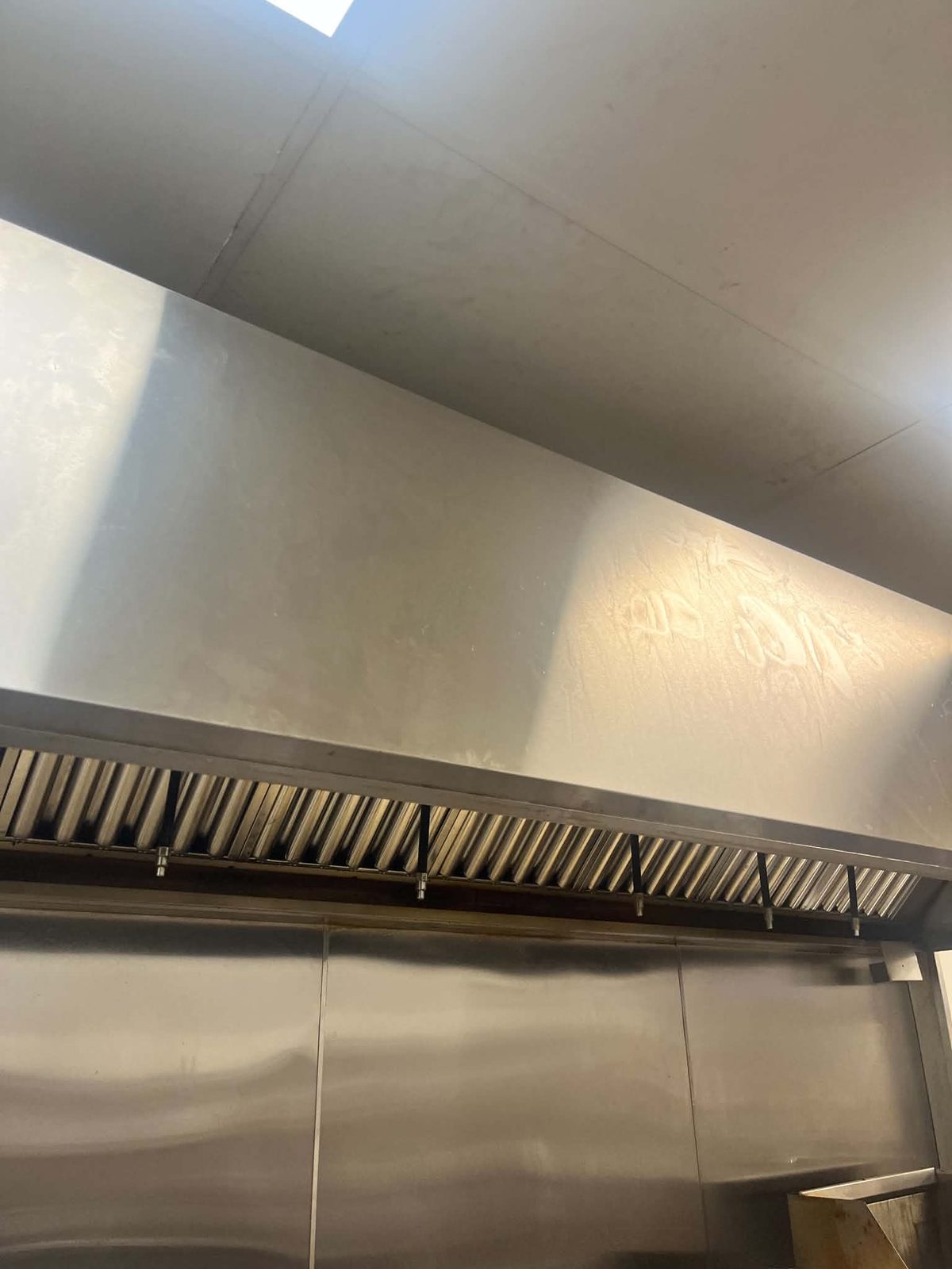 A commercial kitchen hood canopy and stainless steel baffle filter bank after cleaning, showing clean bare metal throughout
