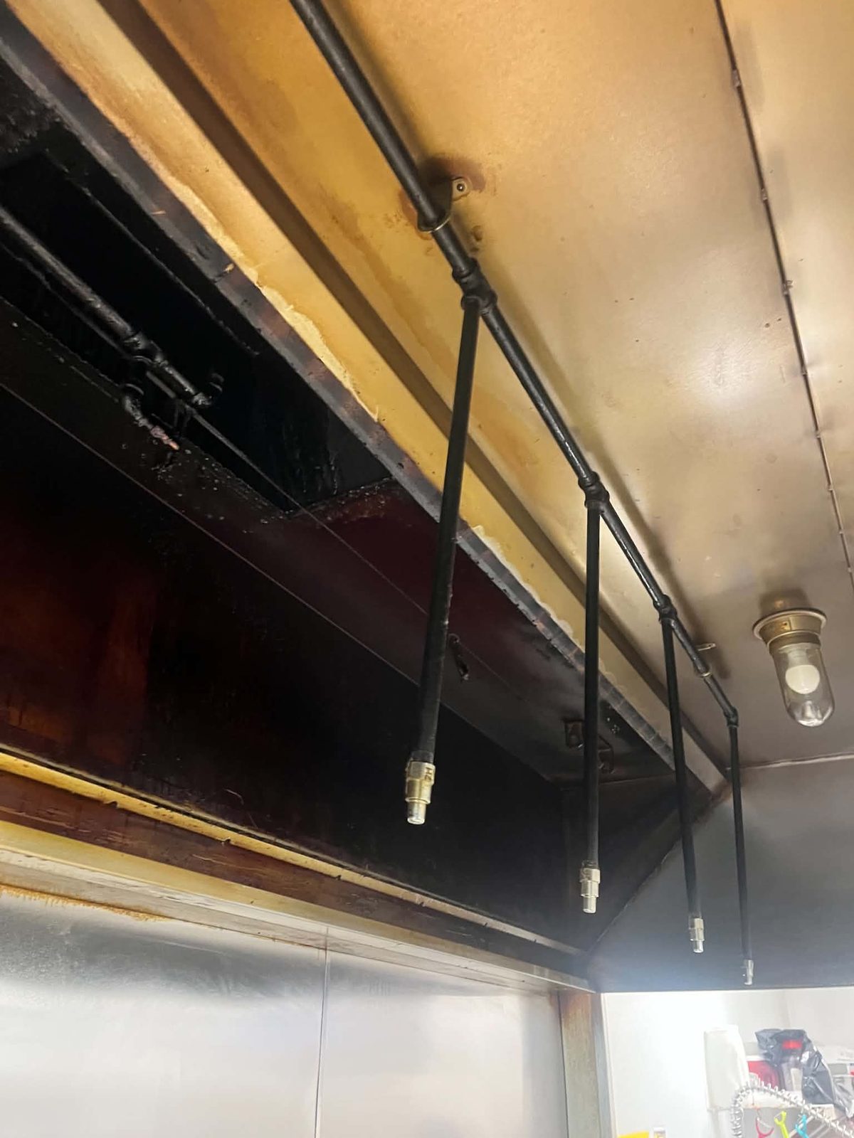 The underside of a commercial kitchen hood coated in thick, hardened brown and black grease, with the ceiling above it stained yellow