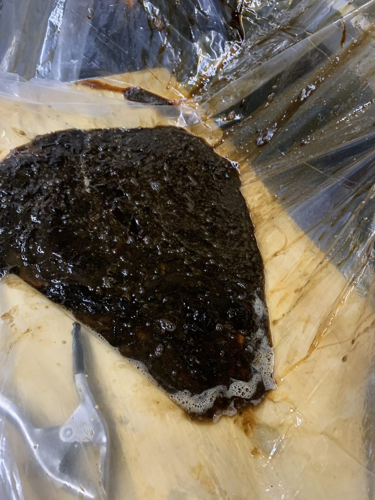 A large mass of black grease sludge collected on plastic containment sheeting after being removed from a kitchen exhaust system
